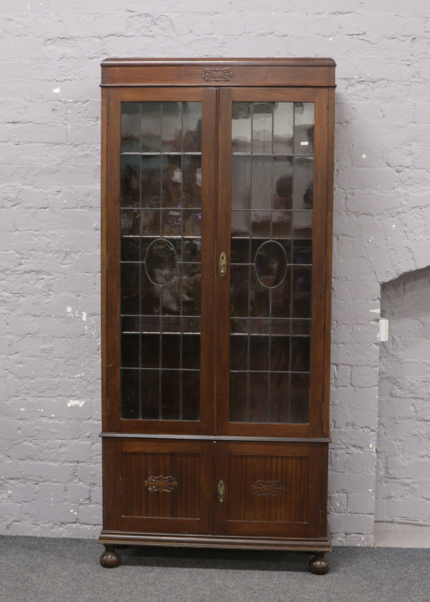 A George V carved oak bookcase with lead glazed doors, raised on turned bun feet, 86cm Wide x 32cm