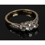 An 18ct gold and platinum three stone diamond ring with diamond set shoulders, size M1/2.