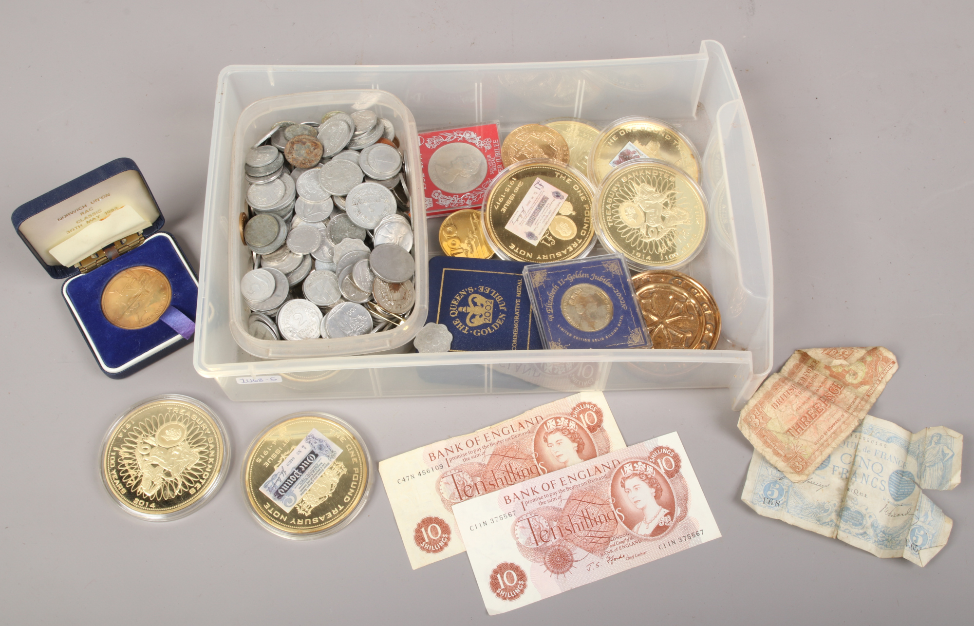 A box of coins and bank notes to include large gilt coins, 10 shilling note, foreign coin examples