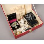 A red leather effect jewellery box containing various dress jewellery including simulated pearl