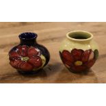 Two Moorcroft squat vases both in The Clematis design, one over yellow ground the other on ink