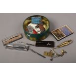 A tin of collectables including pens advertising tins, Zippo lighter, watch cogs and erotic bottle