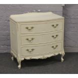 A cream painted bow front chest of three drawers, raised on squat cabriole legs with gilt