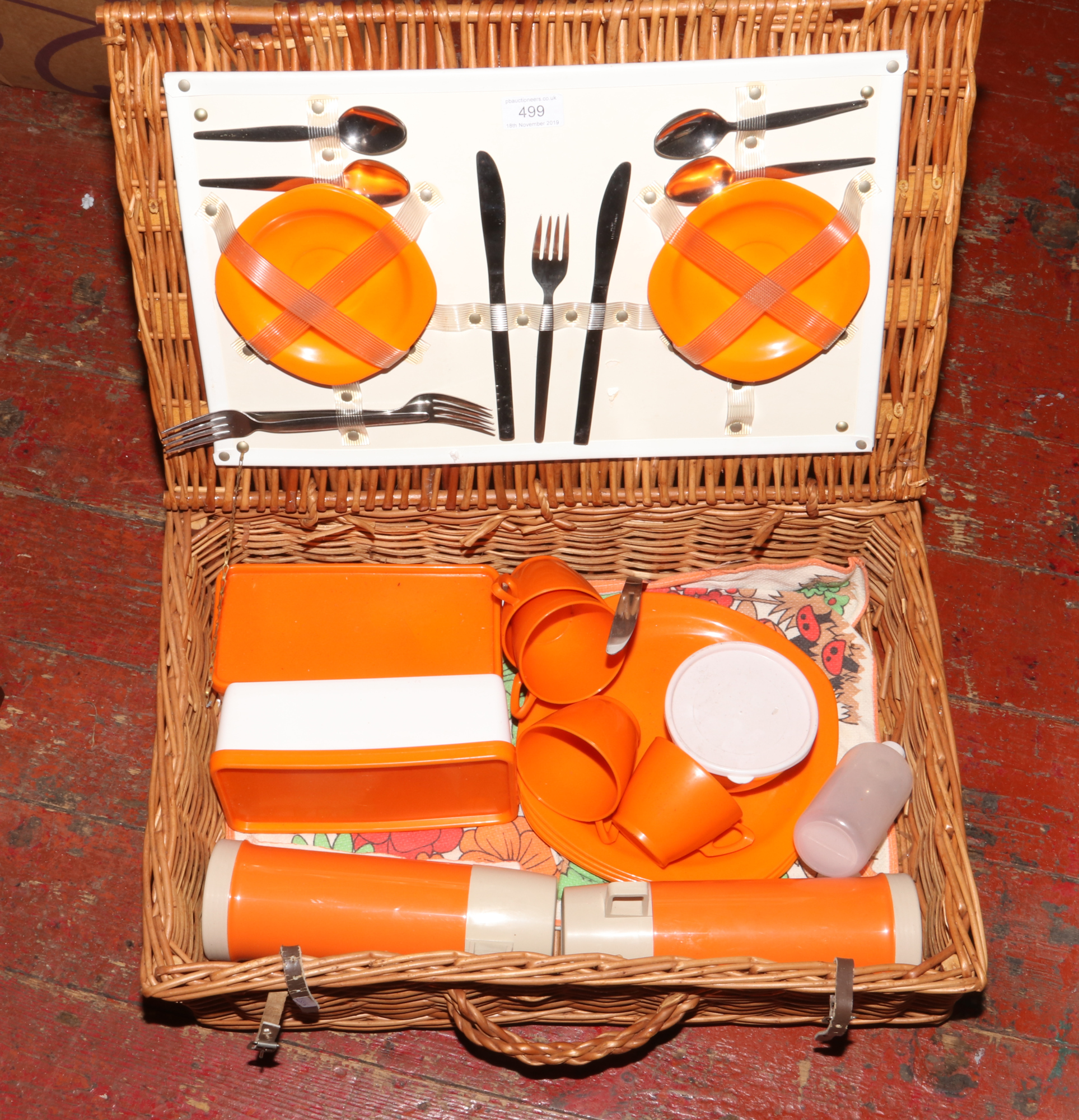 A wicker picnic hamper with contents of stainless steel cutlery and food storage containers.