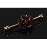 A boxed Victorian yellow metal bar brooch set with a cluster of red faceted stones.