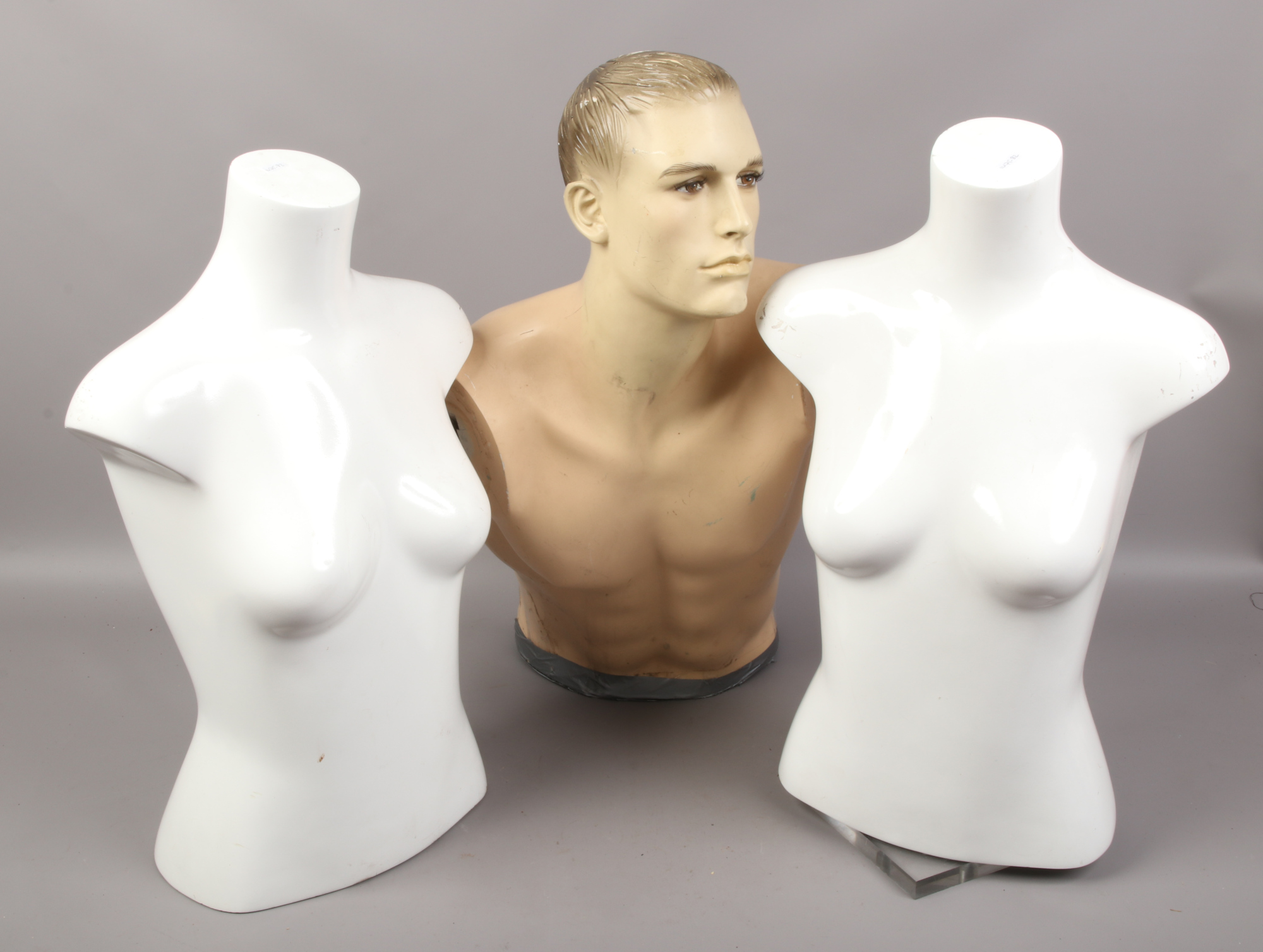 Three upper torso shop mannequins one on rotating base.