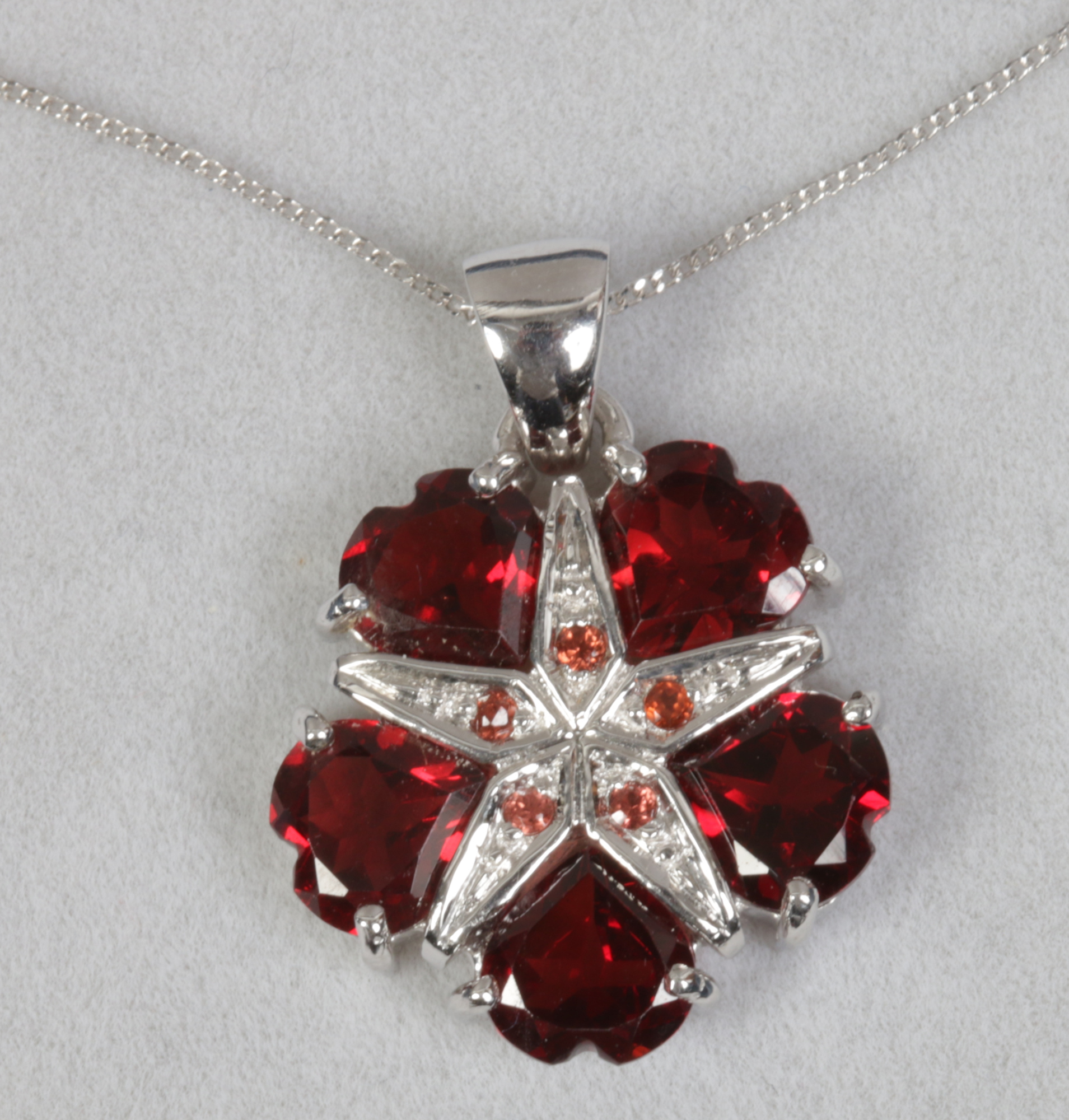 A 9ct white gold and mozambique garnet floriform pendant on chain with heart cut stones.