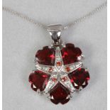 A 9ct white gold and mozambique garnet floriform pendant on chain with heart cut stones.