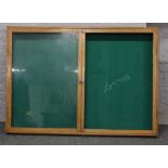 A large oak framed two door wall mounting display cabinet or noticeboard, 140cm wide, 99cm high.