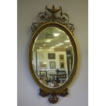 19th Century gilt framed oval wall mirror, with urn, swag and scrolled leaf cresting, bevelled