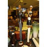 Carved elongated wooden figures of a butler and maid in the style of Jack Vettriano