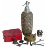 Soda syphon chrome with clear glass body, covered with wire-work, red metal tin containing "
