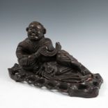 An Oriental hardwood model, of a recumbent figure, with two bats, on a carved wooden base, 9ins x