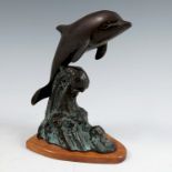 A bronze coloured metal model, of a dolphin jumping through the waves, on a wooden base, height