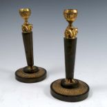 A pair of gilt metal candlesticks, decorated in the Egyptian style with masks, raised on a
