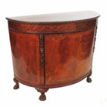 A mahogany D shaped commode, having a central door opening to reveal a shelf, raised on carved