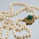A two row uniform cultured pearl necklace, to an emerald and diamond clasp of abstract design, the