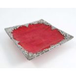 A square coral coloured dish, the edges mounted with embossed white metal, decorated with scrolls