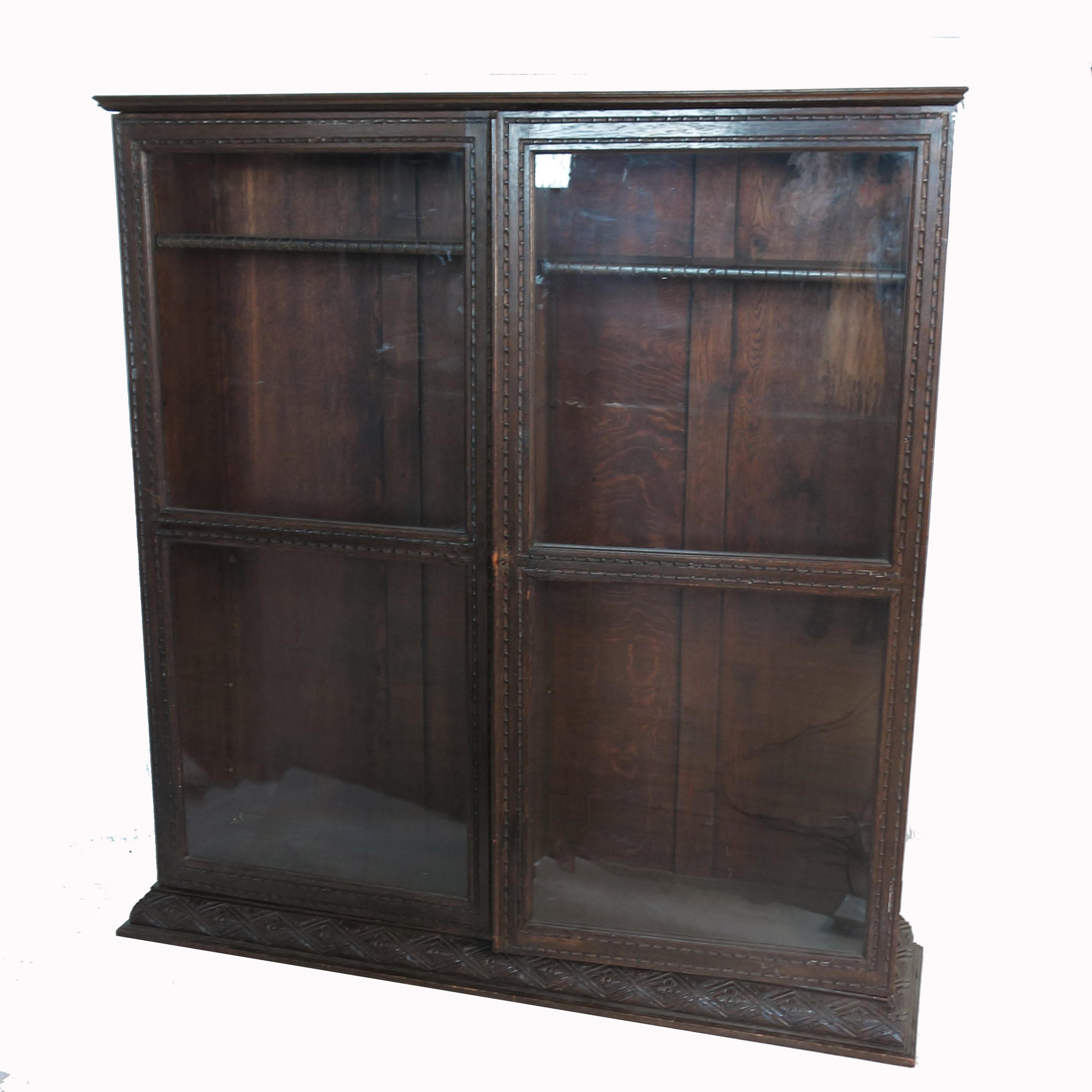 An oak two door glazed bookcase, with carved decoration and adjustable shelves, raised on a plinth
