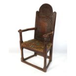 An Antique oak open armchair, with carved solid back, the seat with tapestry upholstery, raised on