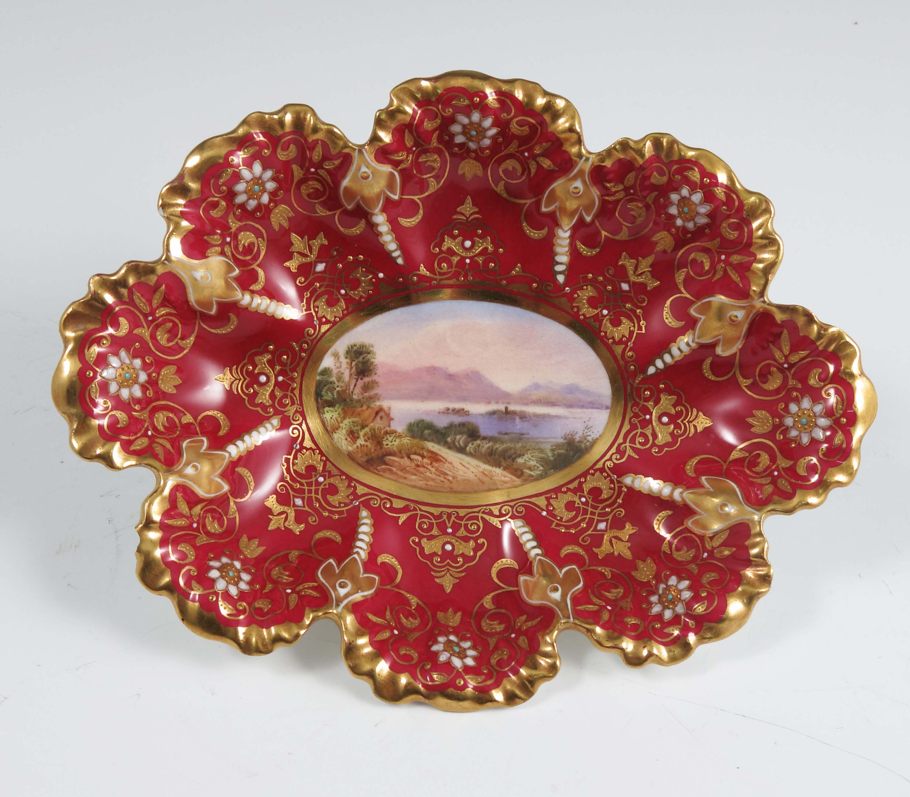 An oval Coalport dish, decorated with a central panel of a lake scene with buildings and