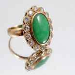 A jade and diamond cluster ring, stamped '18ct', the oval shallow cabochon enclosed by fourteen