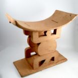 A 20th century tribal stool, with curved seat, raised on a pierced column with rectangular base