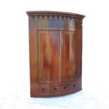 A Georgian mahogany bow fronted corner cupboard, with two cross banded doors, fitted with a drawer