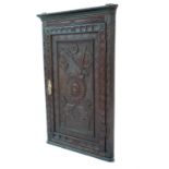 A Georgian oak corner cupboard, having a panel door with later carving, opening to reveal shaped