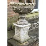 Two garden urns, with embossed Classical decoration, raised on a pedestal mounted on a rectangular