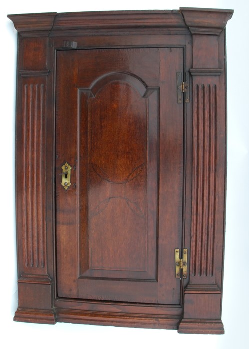 An antique oak corner cupboard, the door having field panel decoration, opening to reveal fitted