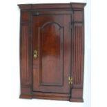 An antique oak corner cupboard, the door having field panel decoration, opening to reveal fitted