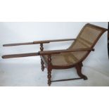 A mahogany and cane plantation armchair, having swivel extensions to the arms, scroll back and seat,