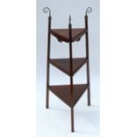 An Arts and Crafts walnut tapered triangular three tier stand, with curly brass finials and having