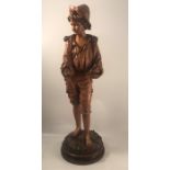 A late 19th century carved wood figure, of a young boy standing, with primitive clothes and a wool