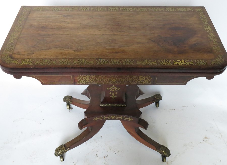 A 19th century rosewood and cut brass fold over games table, raised on an inlaid column to a