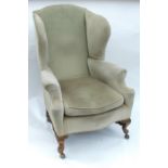 A wing back upholstered armchair, raised on front cabriole legs united by a turned stretcher