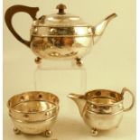 A silver Arts and Crafts three piece tea set, with hammered finish and a band of roundels, raised on