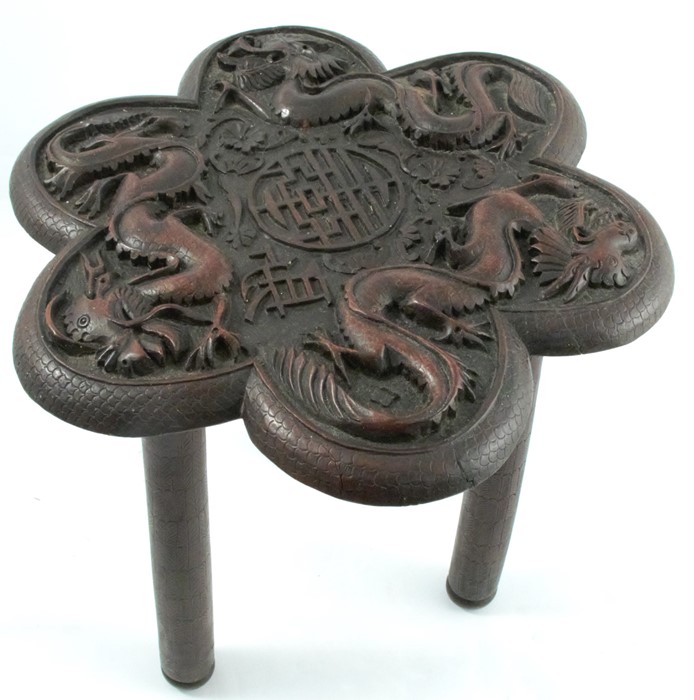 An Oriental wooden table, the shaped top carved with dragons and a motif to the centre, raised on