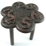 An Oriental wooden table, the shaped top carved with dragons and a motif to the centre, raised on