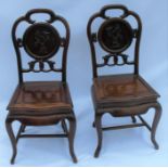 A pair of Oriental hardwood chairs, with carved decoration to the backs, solid seats, raised on