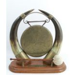 A 19th century table gong, the brass gong supported on a pair of horns, on an oak plinth with