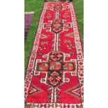 An Eastern style runner, the red ground field decorated with three repeating motifs, 140ins x 35ins