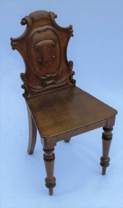 A 19th century oak hall chair, with shield shaped carved back, solid seat, raised on turned front