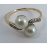 A two stone pearl cross over ring, the yellow shank unmarked, with rose diamond set shoulders, the