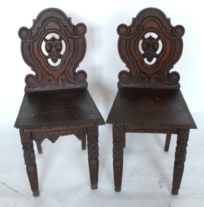 A pair of 19th century hall chairs, the shield shaped back carved with a mask, having solid seats
