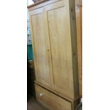 A pine wardrobe, having a pair of fielded doors opening to reveal a hanging space, with bazle drawer