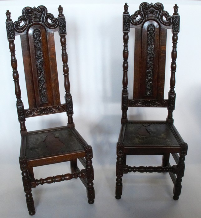 A pair of Antique oak high back chairs, with carved decoration, with leather cover to the solid