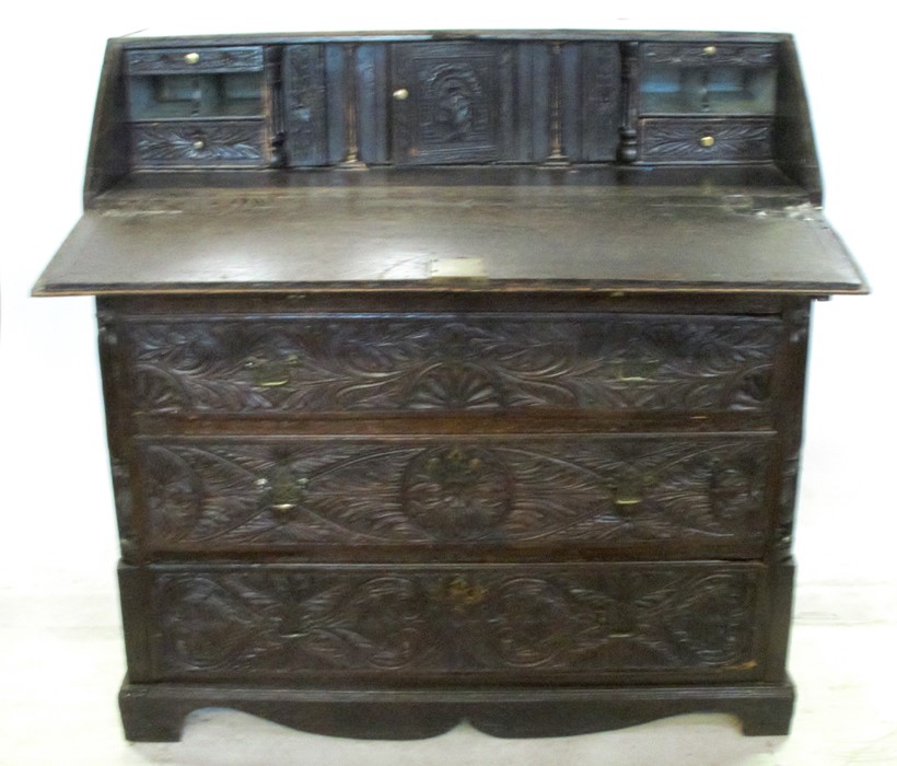 An Antique dark oak carved bureau, the fall flap opening to reveal drawers, cupboard and pigeon