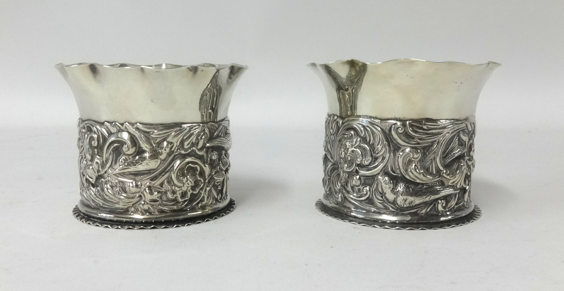 A pair of Edwardian silver pots, William Comyns London, height 7cm with embossed decoration of birds